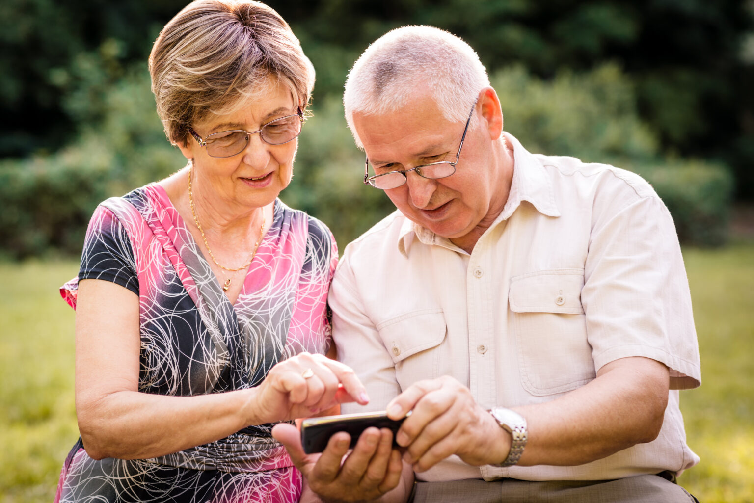 Senior couple looking together on photos in smartphone - outdoor in nature